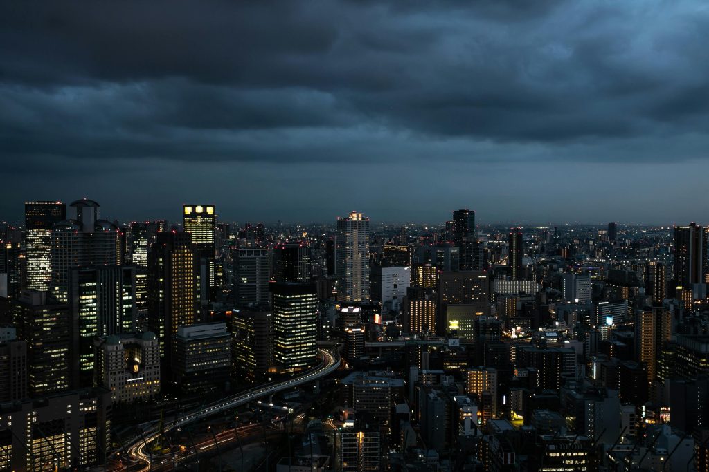 Dramatic Osaka skyline at twilight, showcasing illuminated skyscrapers against moody clouds.